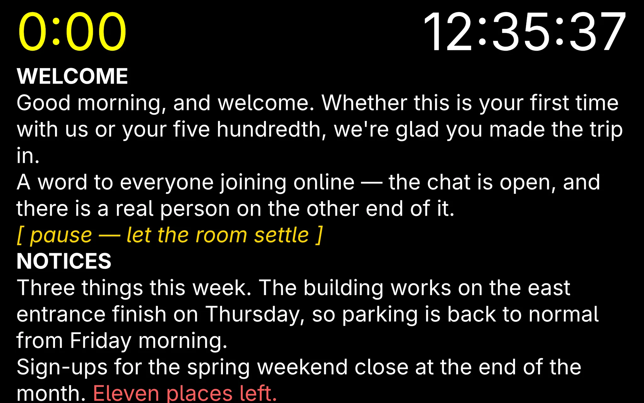 A viewer display: large white text on black, a yellow countdown top left and the time of day top right, with one stage direction picked out in yellow and an urgent notice in red.